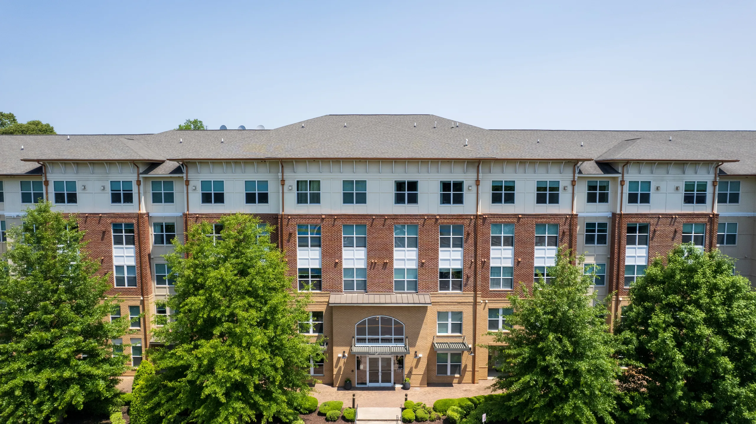 Brick and cream facade of the apartment building framed by mature trees