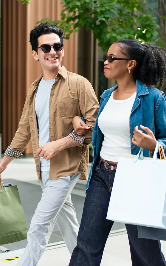 a young man and a young woman lock arms while walking with shopping bags